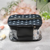 پشت کیف آرایشی زنانه با طراحی ترکیبی مشکی و شفاف، دارای زیپ فلزی با آویز برگ و لوگوهای سفید و مشکی، مناسب برای نگهداری لوازم آرایشی در سفر یا استفاده روزمره