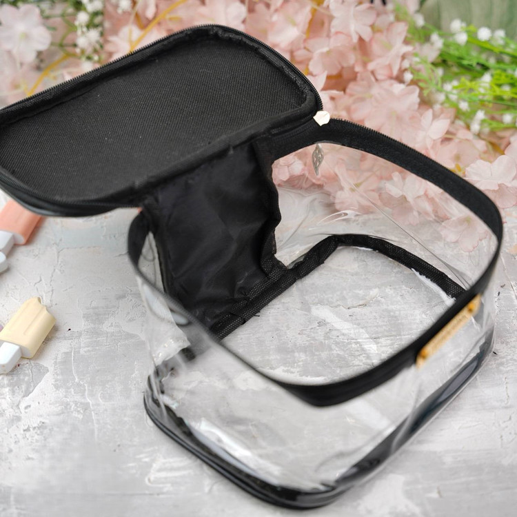 کیف آرایشی زنانه شفاف با زیپ مشکی و فضای داخلی طلقی، مناسب برای نگهداری لوازم آرایشی در سفر یا استفاده روزمره، با زمینه تزئینی شامل گلهای صورتی و آیتمهای آرایشی