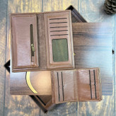 کیف پول و جاکارتی چرمی طبیعی قهوهای با طراحی داخلی، قرارگرفته روی سطح چوبی با تزئین طلایی
