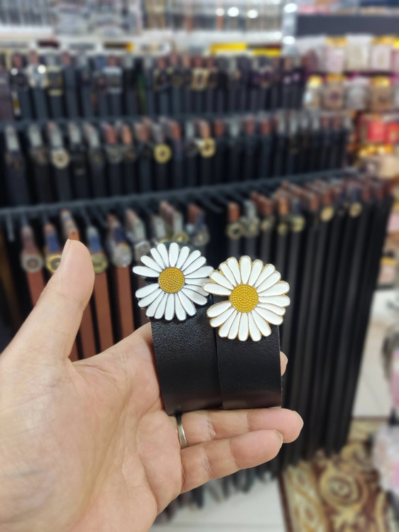 کمربند زنانه چرم مصنوعی مشکی با سگک بابونه، نمایش در ویترین فروشگاه و روی دست خریدار