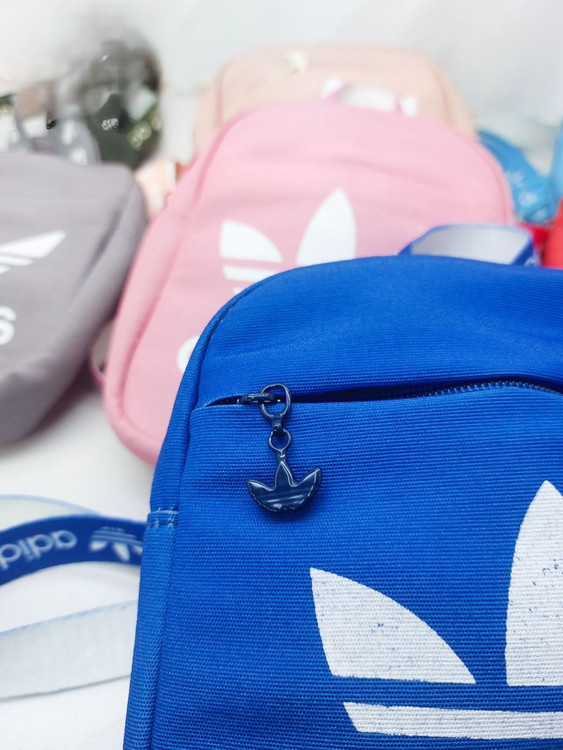 بادی بگ آبی آدیداس با سرزیپ و بند برند آدیداس، همراه با مدلهای صورتی، طوسی و کرم در پسزمینه